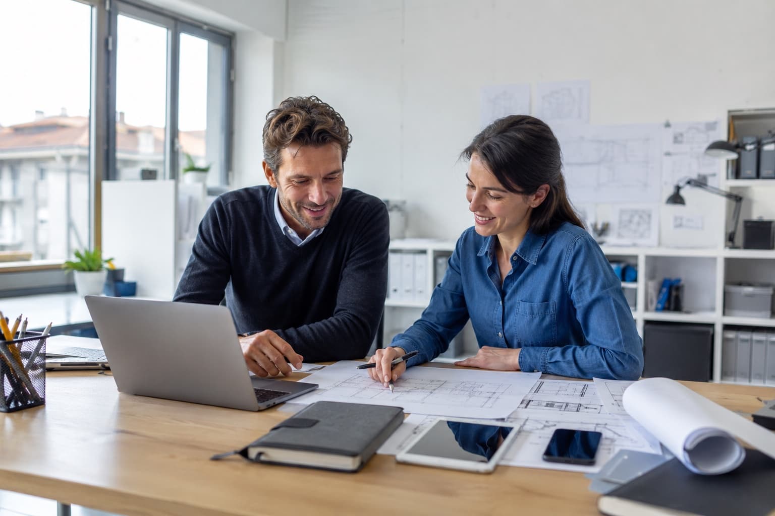 Due professionisti tecnici lavorano insieme su laptop e planimetrie in uno studio luminoso
